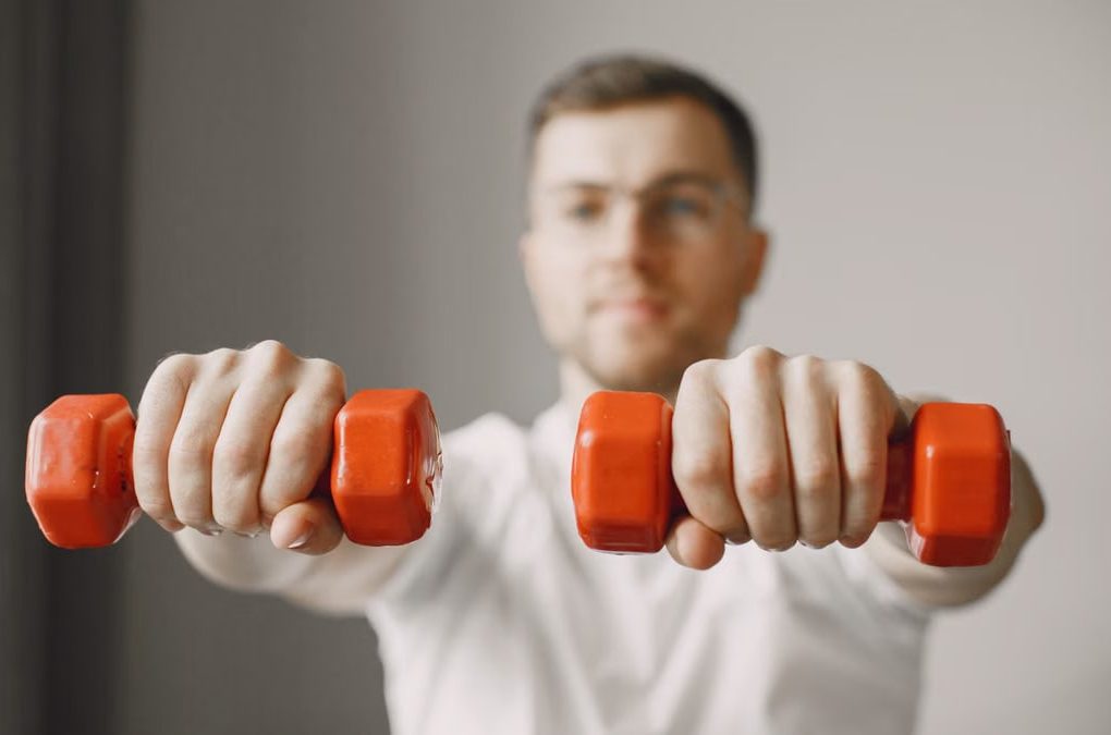 Focused adult male exercising with red dumbbells at home, promoting a healthy lifestyle.