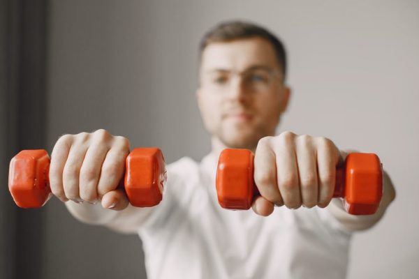 Focused adult male exercising with red dumbbells at home, promoting a healthy lifestyle.