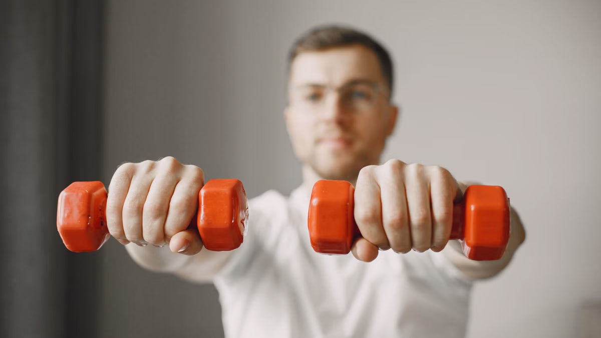 Focused adult male exercising with red dumbbells at home, promoting a healthy lifestyle.